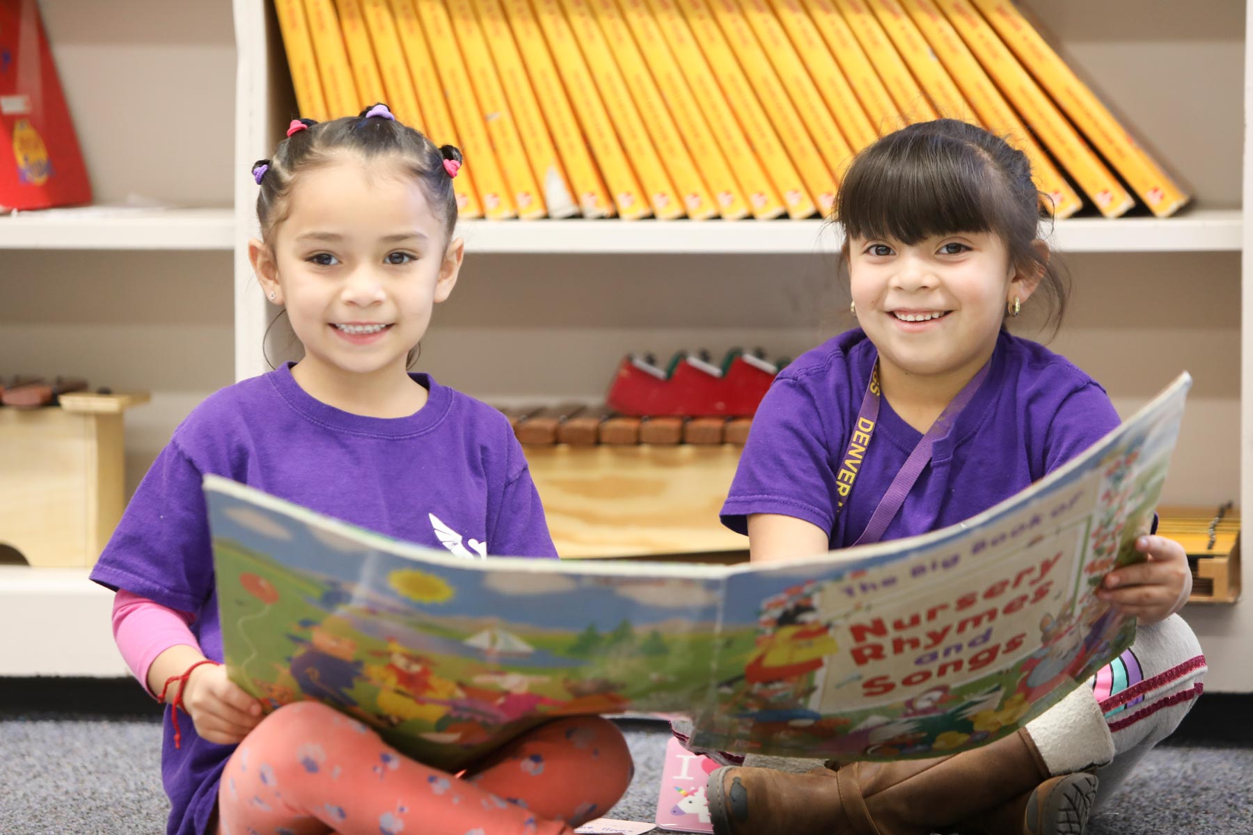 Two students smiling at the camera while holding a book in class